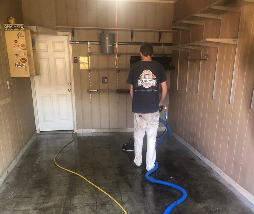 Person using a carpet cleaning machine in a garage setting, emphasizing professional cleaning services for home health and cleanliness.